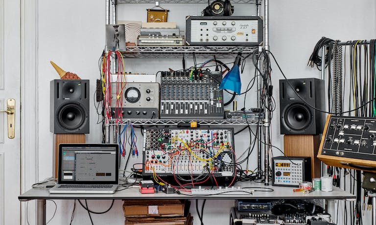 A creative space with a modular synth setup and Ableton Live running Max for Live on the screen.