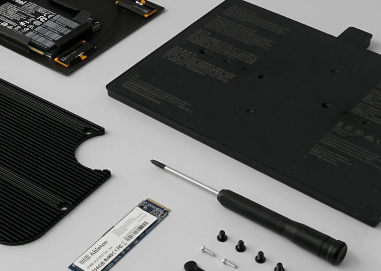The upgrade kit contents, neatly arranged on a surface – the processor, hard drive, battery and heatsink, along with a screwdriver and a variety of screws.
